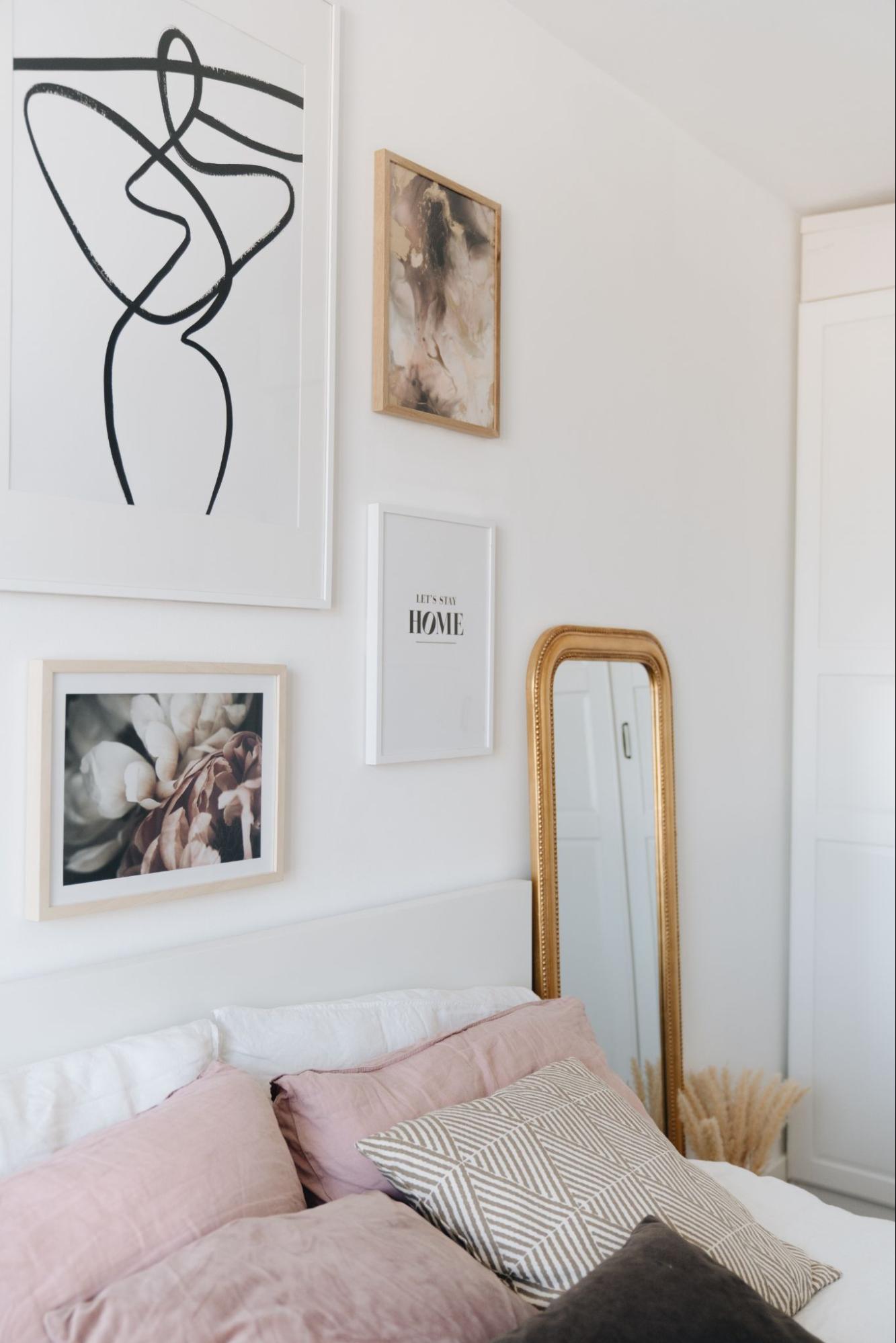 Łóżko w sypialni z białymi ścianami, na ścianie są jasne, eleganckie plakaty