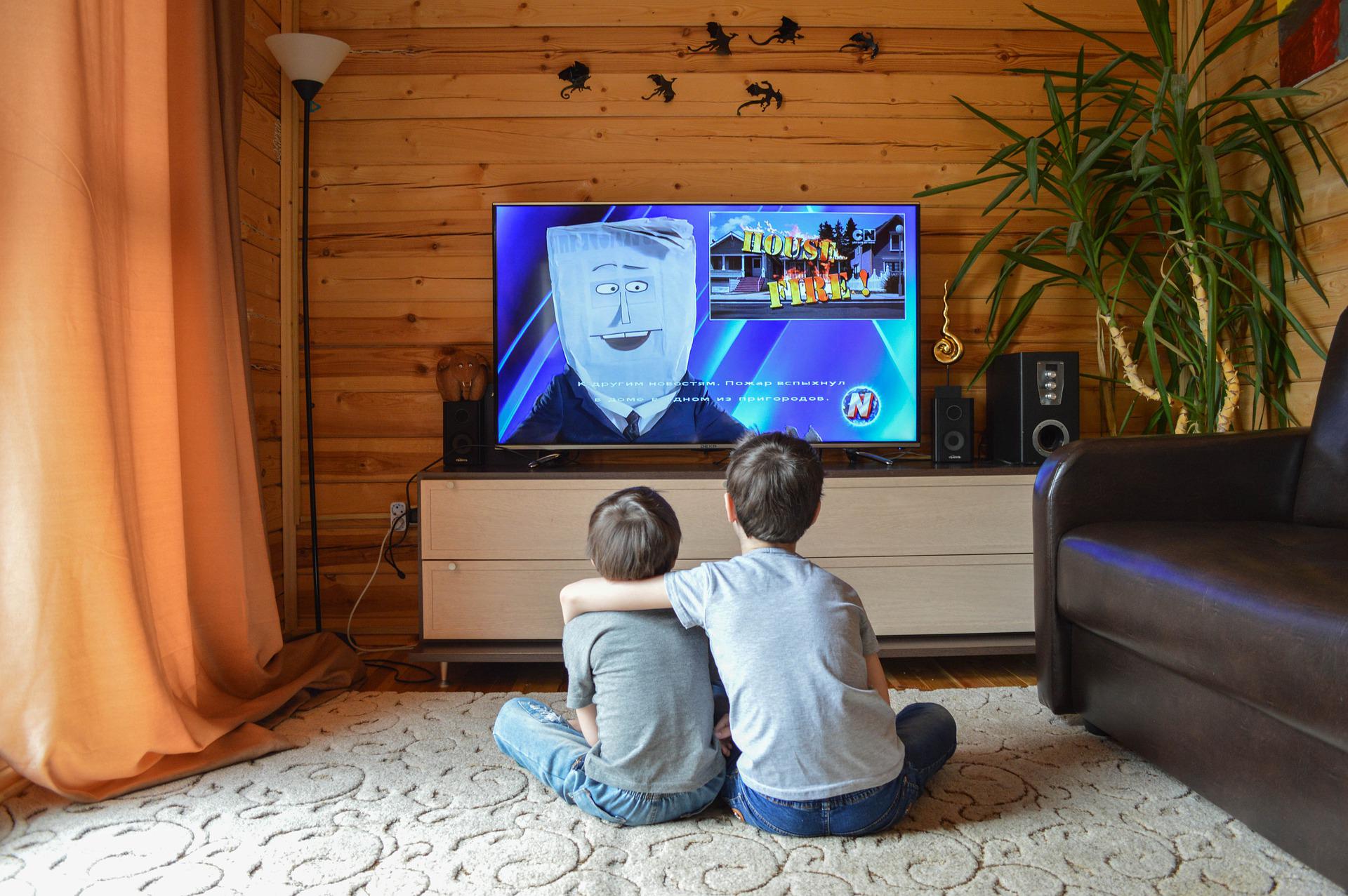 Dwaj chłopcy oglądają kreskówkę w pokoju, na ścianie są grafiki latających smoków.